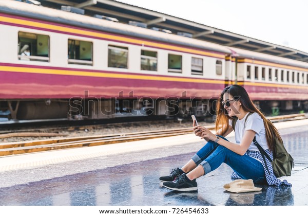 Asian tourist teenage girl at train station using\
smartphone map, social media check-in, or buy ticket booking.\
Modern travel app technology, lone traveler, Summer vacation\
railroad adventure\
concept