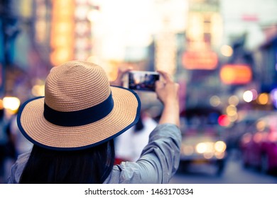 Asian tourist wearing hat is taking pictures with bokeh street lights, a woman wearing a hat, using a photo tablet, Yaowarat Road, beautiful bokeh at Yaowarat Road, Thailand.
