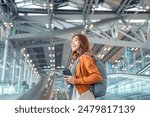 Asian tourist woman traveller with backpack holding mobile phone while stand on moving walkway in airport terminal, Tourist journey trip concept.