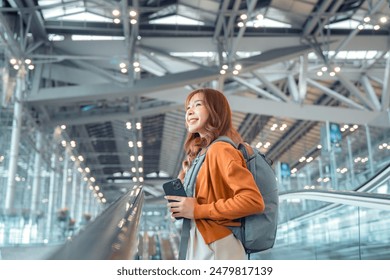 Asian tourist woman traveller with backpack holding mobile phone while stand on moving walkway in airport terminal, Tourist journey trip concept. - Powered by Shutterstock