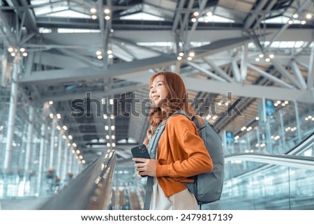 Asian tourist woman traveller with backpack holding mobile phone while stand on moving walkway in airport terminal, Tourist journey trip concept.
