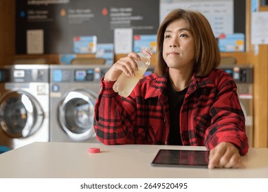 Asian transgender non-binary individual sitting in a modern laundromat laundry shop