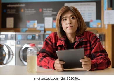 Asian transgender non-binary individual sitting in a modern laundromat laundry shop