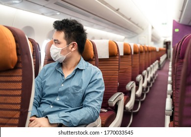 Asian Traveler Business Man With Sitting On Aisle Seat Wearing Face Mask Looking Out Of Window On Airplane In Airport. Male Passenger Traveling By Plane Transportation During Covid19 Virus Pandemic.