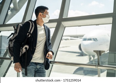 Asian Traveler Business Man Wearing Face Mask Waiting To Board Into Airplane, Standing In Departure Terminal In Airport. Male Passenger Traveling By Plane Transportation During Covid19 Virus Pandemic.