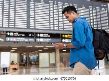 Asian Traveler Using The Smart Mobile Phone For Check-in At The Flight Information Screen In Modern An Airport, Travel And Transportation With Technology Concept.