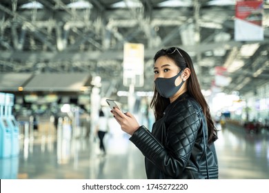 Asian Traveler Woman With Luggage, Bag Wearing Face Mask, Hold Phone At Departure Check In Airport Terminal. Smart Female Passenger Traveling By Plane Transportation During Covid19 Virus Pandemic.