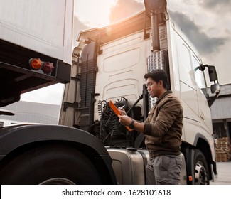 Asian truck driver holding clipboard inspecting safety vehicle maintenance checklist of modern semi truck.