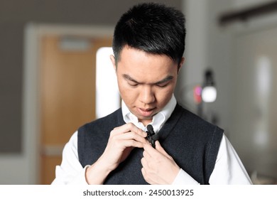 An Asian tutor is adjusting his lavalier microphone for a online class over video inside the recording studio - Powered by Shutterstock