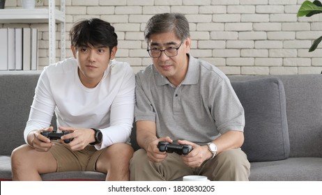 Asian two age generations men family old father embracing young adult son having fun enjoying play video game funny video using at home sit on sofa. Happiness Asian family concepts. - Powered by Shutterstock