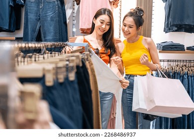 Asian two beautiful women looking at clothes product in shopping mall. Attractive happy girl enjoy walking in department store to choose dress and new t-shirt from clothing racks in marketplace center