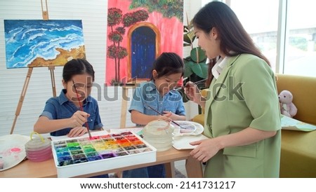 Asian two siblings learning study watercolor paint together at home. Teacher or parent teach student or daughter drawing paint color imagination on paper homework.Activity creativity education concept