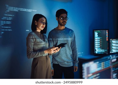 Asian Two software developers engaged in collaborative coding session, with code projected onto the wall and multiple computer screens displaying