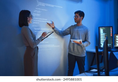 Asian Two software developers presentation in collaborative coding session, with code projected onto the wall and multiple computer screens displaying