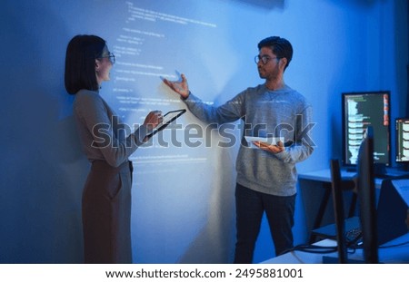 Asian Two software developers presentation in collaborative coding session, with code projected onto the wall and multiple computer screens displaying