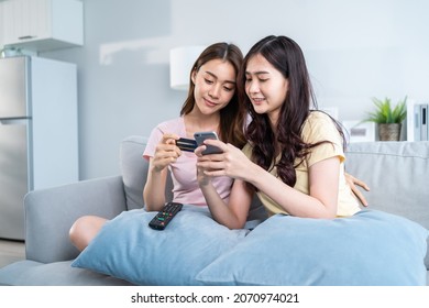 Asian two woman friend enjoy shopping online in living room at home. Beautiful lesbian couple sit on sofa, holding credit card to make e bank online payment after use phone purchase goods in web store - Powered by Shutterstock