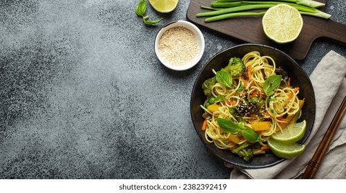 Asian vegetarian noodles with vegetables and lime in black rustic ceramic bowl, wooden chopsticks, cutting board with chopped green onion top view, stone background. Cooking noodles, copy space - Powered by Shutterstock