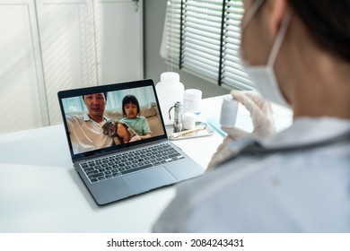 Asian Veterinarian Girl Talk To Pet Owner On Online Virtual Video Call. Professional Vet Doctor Woman Use Laptop Computer To Give Treatment Plan Consult For Little Cat Animal While Sit In Pet Hospital