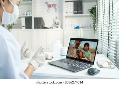 Asian Veterinarian Girl Talk To Pet Owner On Online Virtual Video Call. Professional Vet Doctor Woman Use Laptop Computer To Give Treatment Plan Consult For Little Cat Animal While Sit In Pet Hospital