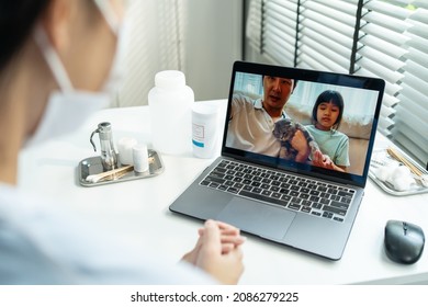 Asian Veterinarian Girl Talk To Pet Owner On Online Virtual Video Call. Professional Vet Doctor Woman Use Laptop Computer To Give Treatment Plan Consult For Little Cat Animal While Sit In Pet Hospital