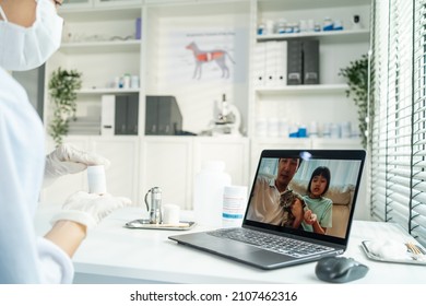 Asian Veterinarian Girl Talk To Pet Owner On Online Virtual Video Call. Professional Vet Doctor Woman Use Laptop Computer To Give Treatment Plan Consult For Little Cat Animal While Sit In Pet Hospital