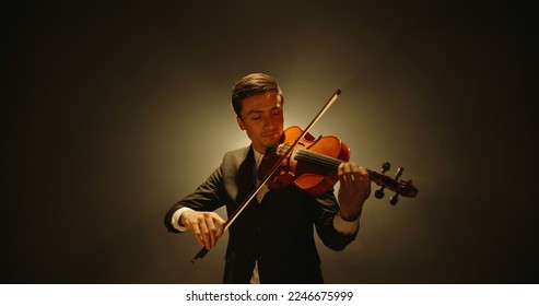 Asian violinist performing on stage. Popular musician playing solo on his his instrument on smoked black background  - Powered by Shutterstock