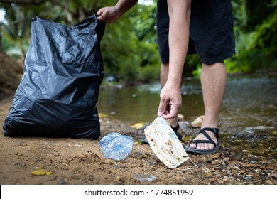 Asian volunteer is picking up trash waste rubbish with garbage bag,medical masks of tourists in national park,problem of littering the face mask during its reopening after COVID-19 quarantine
