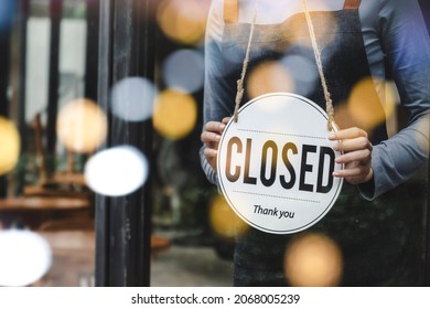 asian waitress staff woman wearing apron turning CLOSED sign board on glass door with bokeh light in modern cafe coffee shop, cafe restaurant, retail store, small business, food and drink concept