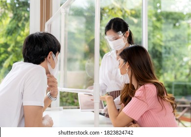 Asian Waitress Wear Face Mask And Face Shield Using Tablet To Show Restaurant Electronic Menu And Recommend To Couple Customers. New Normal Technology And Lifestyle Food And Dining Concept.