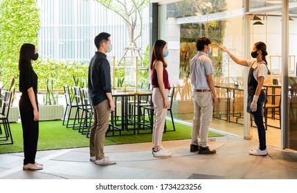 Asian Waitress Wear Protective Face Mask Scan Customer Temperature By Thermometer Before Entering The Restaurant To Protect Infection From Coronavirus Covid-19, Social Distancing Concept
