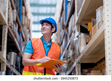 Lagerarbeiter oder Fabrikarbeiter mit blauem hartem Hut und gleichem Ständer zwischen den Regalen am Arbeitsplatz. Konzept des guten Managements und der Zufriedenheit der Mitarbeiter während der Arbeit in der Industrie.