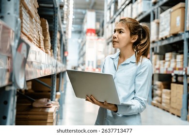 Asian warehouse worker checking inventory using laptop computer for stock management and logistics control in modern storage facility, digital transformation in supply chain business.