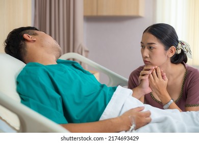 Asian Wife Holding Hand And Look Worried And Sad Of Husband Sickness. Patient Male Sleeping In Hospital Ward. Family Support, Life Insurance, Healthcare And Medical