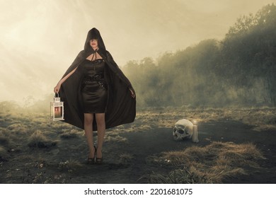 Asian witch woman with a black cloak holding a lantern standing on the field with the dramatic scene background - Shutterstock ID 2201681075