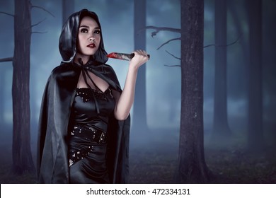 Asian witch woman holding 
bloodstained knife in forest with fog background