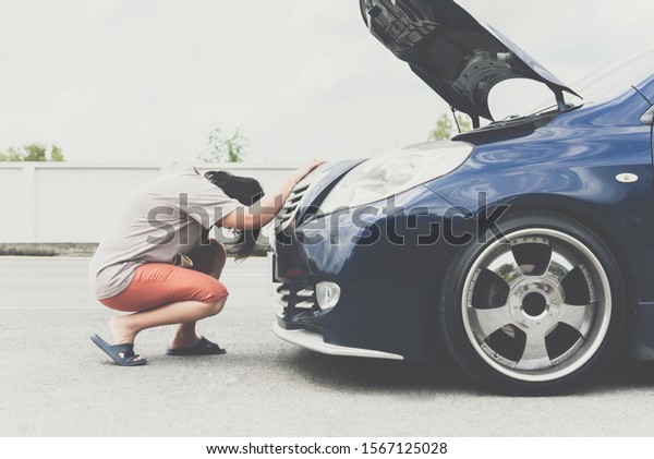Asian woman 40s alone\
driver checking a car engine for fix and repair problem with\
unhappy and dismal between waiting a car mechanic from car engine\
problem at roadside
