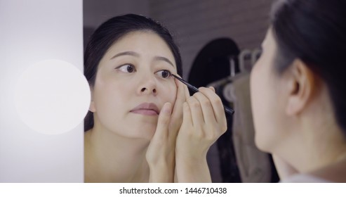 Asian Woman Actress Getting Ready Applying Black Eyeliner Eye Pencil On Eyes Looking In Mirror Of Vanity Table. Reflection Of Gorgeous Lady Performer Doing Makeup In Dressing Place In Backstage.