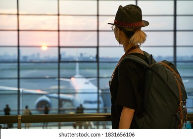 asian woman air traveler looking at sunrise through window while walking in airport terminal building