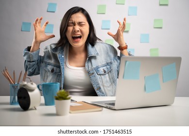 Asian Woman Angry Working On A Laptop And Shouting At Home Office. WFH. Work From Home. Prevention Coronavirus COVID-19 Concept.