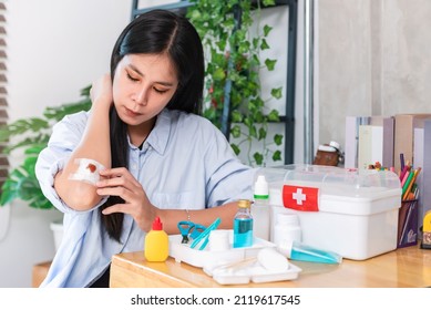 Asian Woman Applying Antiseptic Solution To Wound On Her Elbow, First Aid Kit At Home