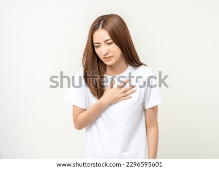 Asian woman around 25 year She felt a pain in her chest held her hand and squeezed it. She had a heart attack that needed treatment. Wearing white shirt standing on isolated background.