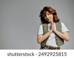 An Asian woman with auburn hair, wearing a vest, poses with her hands clasped in a gesture of grace.