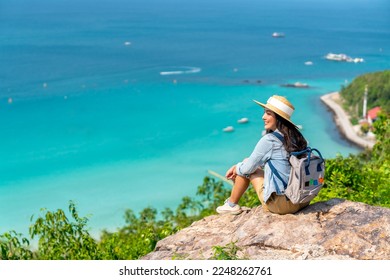 Asian woman with backpack travel at tropical island and resting on mountain peak in summer sunny day. Attractive girl enjoy outdoor lifestyle looking beautiful ocean nature on beach holiday vacation. - Shutterstock ID 2248262761