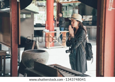asian woman backpacker tourist carrying camera experience japanese traditional culture pray for blessings hand in shitennoji temple. young girl elegant close eyes stand in peaceful shinto osaka japan
