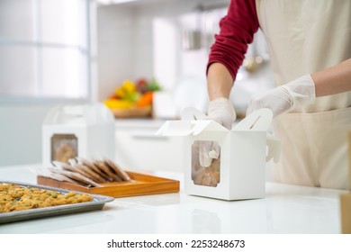 Asian woman bakery shop owner preparing customer order cookie in delivery box on kitchen counter. Woman bakery chef making bakery in the kitchen. Small business entrepreneur and food delivery concept. - Powered by Shutterstock