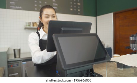 Asian Woman Barista People In Apron Working On POS System Machine With Blank Empty Space Screen Monitor On Counter, Cafe Restaurant Cashier. Waitress In Coffee Shop. People Lifestyle. Business Service