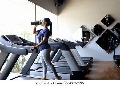 Asian woman with beautiful face drinking water on treadmill machine.  drink supplement drinks when exercising.bcaa, pre-workout drink, protein drink, whey protein milk concept.