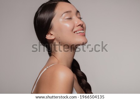 Asian woman with beautiful and healthy skin on beige background. Girl smiling with her eyes closed.