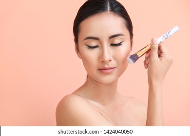 Asian woman with beautiful makeup and brush on color background
