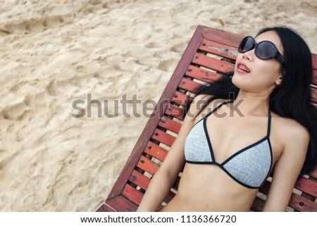 Asian woman in bikini laying on a wooden beach chair at the seaside